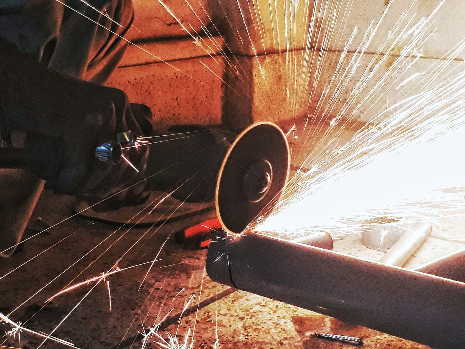 An abrasive wheel cutting through a steel pipe with a wide fan of white sparks