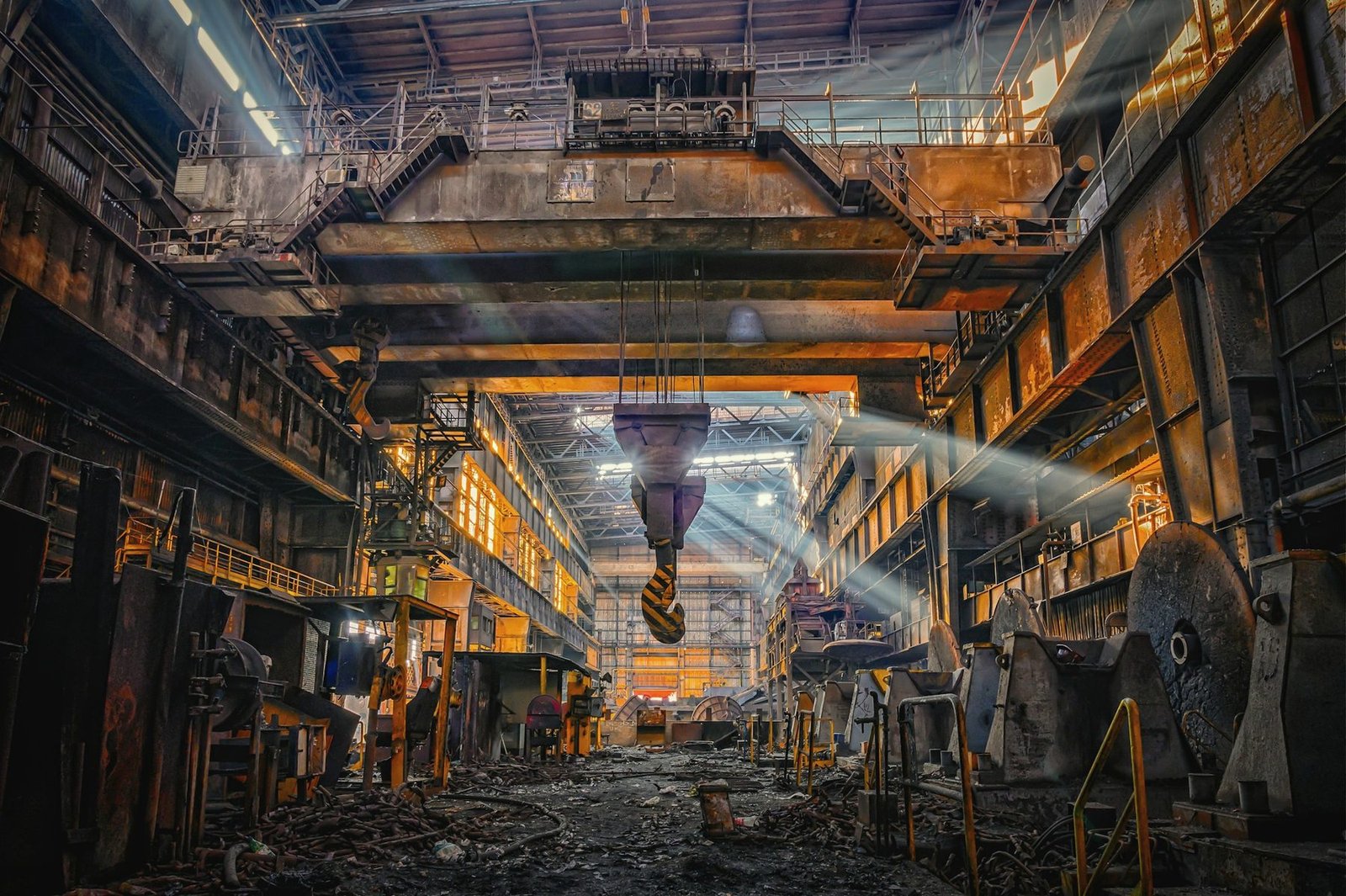 Inside a large old steel mill hall with an overhead crane and hook hanging over the floor