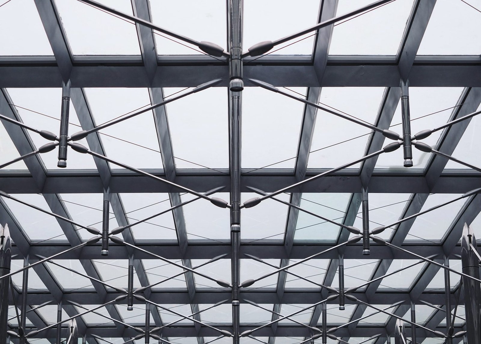 Looking up at a steel roof frame of beams, purlins and cross bracing against a pale sky