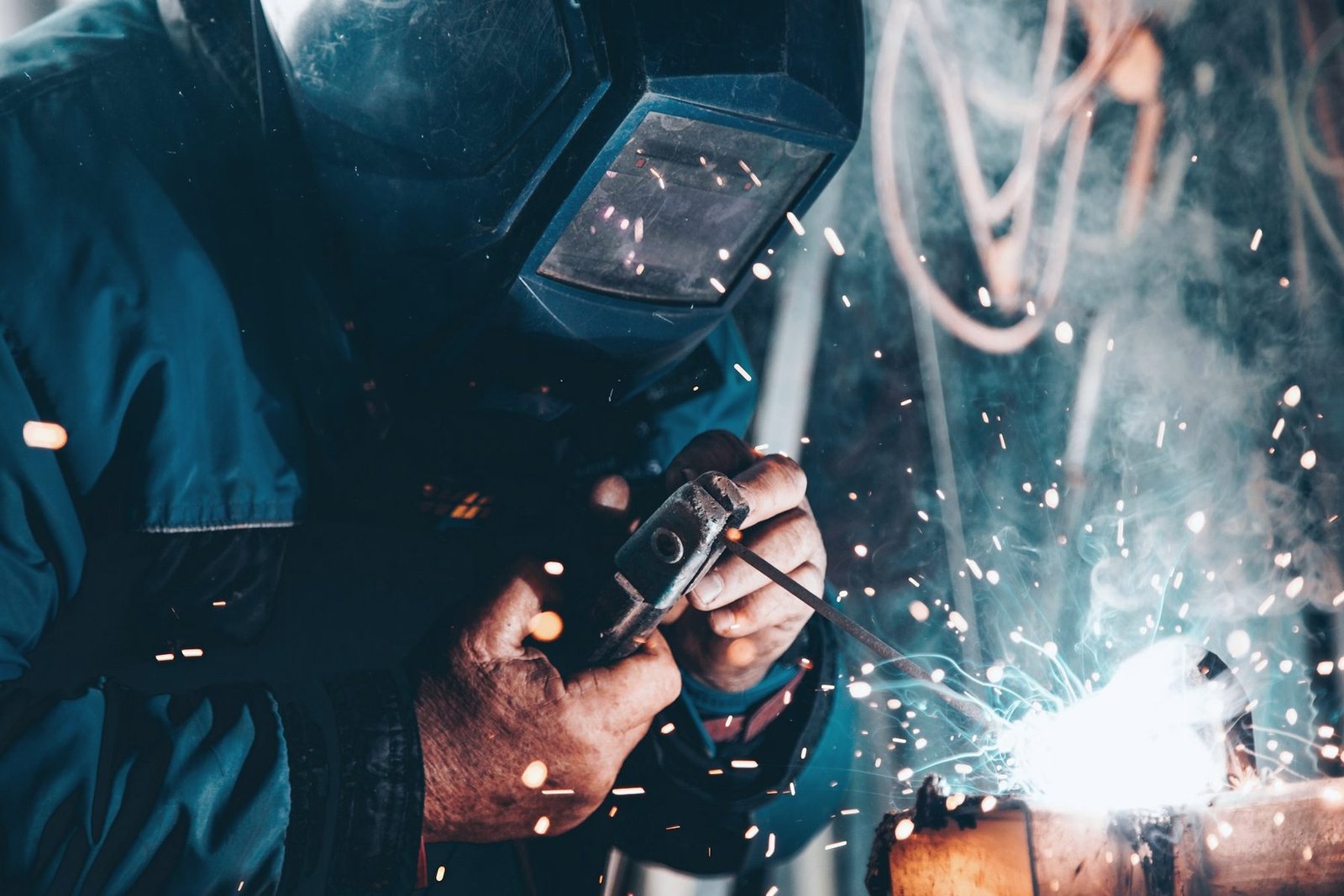 Close view of a welder's hand on a torch trigger with sparks flying off the weld